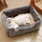 Chat blanc à poils longs allongé dans un panier rectangulaire gris à rebords rembourrés, posé sur un tapis clair.