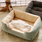 Chat blanc allongé dans un panier vert sauge à intérieur crème et rebords rembourrés, avec un panier gris à l’arrière-plan.